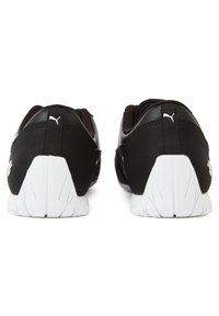 Svarta sportskor med övre del i texturerat tyg och gummisula, med vit yttersula och diskret logotyp på hälen.