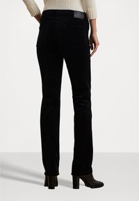 Pantaloni di velluto a coste neri con taglio dritto, dotati di una vita alta e tasche posteriori sottili. Indossati con stivaletti con tacco.