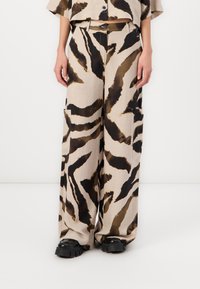 Pantalons large beiges à motif zèbre avec des accents marron, fabriqués en tissu doux, dotés de poches latérales et d'une coupe décontractée.