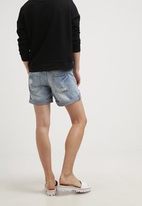 Shorts de mezclilla en azul claro con un diseño desgastado, dobladillos enrollados y dos bolsillos traseros, combinados con una sudadera negra y sandalias blancas.