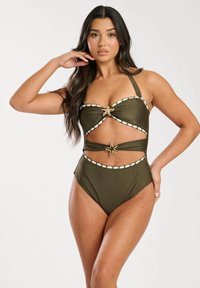 Bikini vert olive avec bretelles à nouer, présentant des détails festonnés blancs et un accent décoratif central. Design découpé avec taille haute.