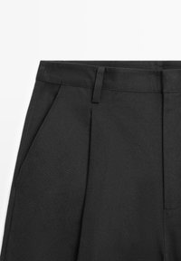 Pantalon noir avec plis, passants pour ceinture et poches latérales, présenté de la taille vers le bas sur un fond blanc.