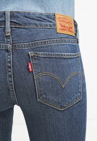Jeans de mezclilla azul oscuro con un diseño distintivo en el bolsillo trasero, que presenta una etiqueta roja de Levi’s y detalles de costura clásica.