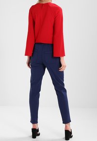 Červený top s dlouhými rukávy, zadním detailem ve tvaru klíčové dírky a zvonovými rukávy, zkombinovaný s navy elastickými kalhotami a černými sandály na silném podpatku.