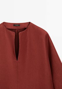 Lněné šaty v rezavé barvě s výstřihem do V, volným střihem a krátkými rukávy. Obsahují centrální šev a minimalistický design.