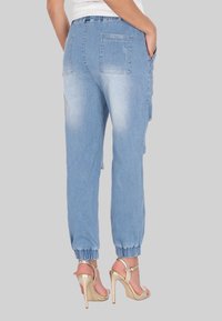 Jasnoniebieskie dżinsowe joggery z elastycznym pasem i ściągaczami, z tylnymi kieszeniami i lekko przetartym wyglądem. Noszone z złotymi szpilkami.