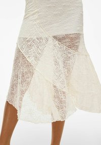 Jupe en dentelle présentant un design asymétrique en couches de couleur blanc cassé, avec des motifs texturés et une matière légère qui tombe avec souplesse.