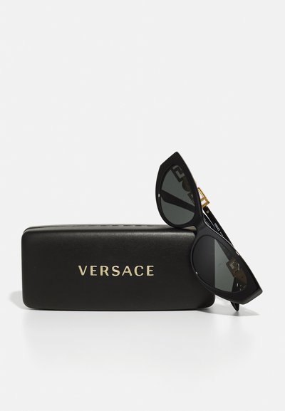 Čierne slnečné okuliare v štýle mačacích očí s tmavými sklami, so zlatými akcentmi a čiernym púzdrom označeným "VERSACE" zlatým písmom.