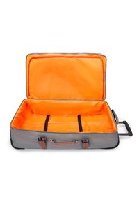Valise souple grise avec un intérieur orange vif, ouverte et vide, montrant des sangles de rangement noires ajustables et une poignée latérale avec une barre de tirage déployée.