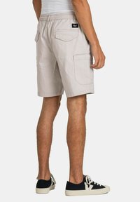 Pantalones cortos cargo beige claro con cintura elástica, bolsillos laterales y un bolsillo parche en la parte trasera. Tejido texturizado con un corte holgado.