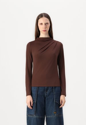 Haut marron à manches longues avec un décolleté drapé, fabriqué en tissu doux. Associé à un pantalon cargo en denim bleu ample avec des poches.