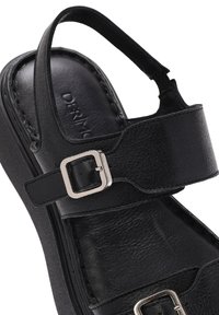 Black leather sandal with a buckle strap, textured insole, and a molded outsole for support. Features an open back design.