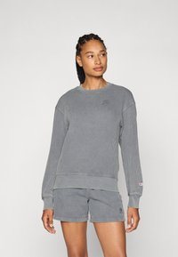 Grå ribbestrikket hettegenser med lange ermer og rund halslinning, kombinert med matchende shorts. Har en liten logo på brystet og låret.