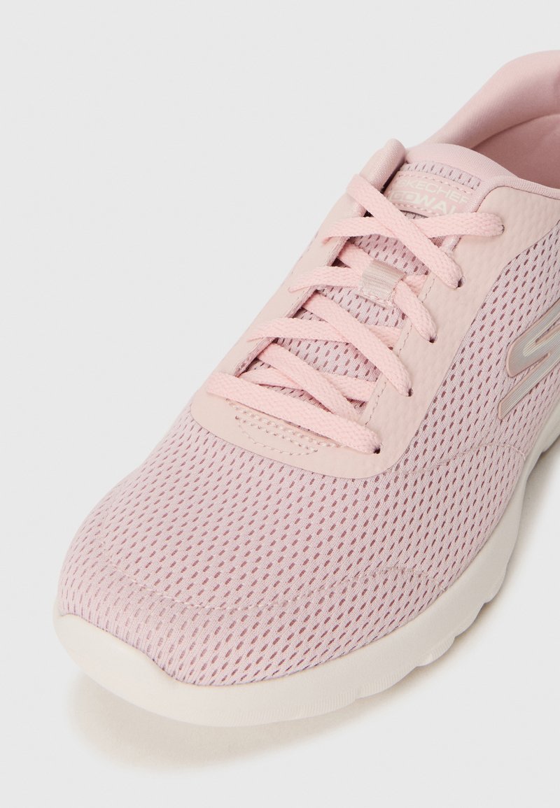 Närbild av en ljusrosa sneaker med ett ventilerande nätöverdrag, med skosnören och en slät sula, som visar upp en modern design.