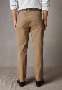 Beżowe bawełniane spodnie o prostym kroju nogawek, z czterema kieszeniami i prostym paskiem w talii. Noszone z czarnymi butami, prezentując gładką teksturę.