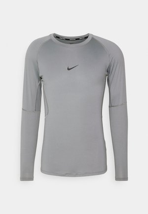 Γκρι αθλητικό μπλούζα με μακριά μανίκια, φτιαγμένη από λείο, υλικό που απορροφά την υγρασία. Έχει επίπεδες ραφές και ένα μικρό μαύρο λογότυπο στο στήθος.