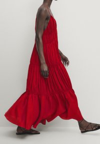 Punainen kerroksellinen maksimekko, joka on valmistettu kevyestä kankaasta. Mekossa on säädettävät spagettiolkaimet, ryppydetalji ja virtaava helma.