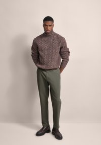 Brown knit turtleneck sweater with a textured pattern, paired with olive green chinos and dark brown lace-up shoes. Neutral background.