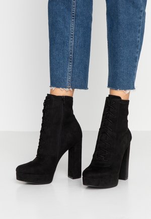 Black suede lace-up platform ankle boots with chunky high heels worn with cropped blue jeans with frayed hems.