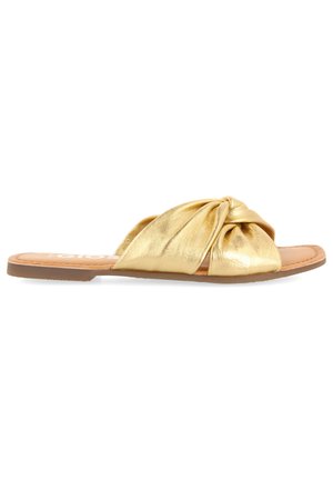 Sandale plate avec bride en cuir doré torsadé et semelle beige, montrée de profil sur fond blanc.