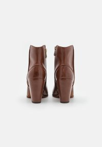 Bottines en cuir marron avec une finition lisse, bout rond et un talon carré de 10 cm. Elles sont dotées d'une fermeture éclair sur le côté pour un enfilage facile.