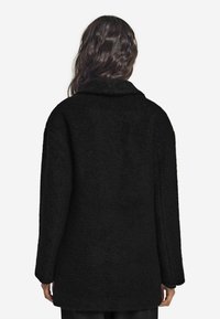 Czarny płaszcz z teksturowanej tkaniny, z szerokim kołnierzem, długimi rękawami i luźnym krojem. Prosty fason bez widocznych zapięć.