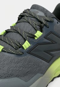 Γκρι αθλητικό παπούτσι με υφή στο επάνω μέρος, μαύρο λογότυπο και φούξια κορδόνια. Διαθέτει μαλακό πέλμα και ενισχυμένη περιοχή στα δάχτυλα.