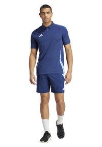 Marineblauwe sportieve polo en korte broek set met lichte blauwe accenten, korte mouwen en een drieknoopsluiting. Het materiaal lijkt lichtgewicht en ademend te zijn.