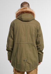 Olivno zelena parka jakna s kapuco obloženo s umetnim krznom, ravno krojena, s pritiskači na robu. Ima ravne šive in odprtino na zadnjem delu.