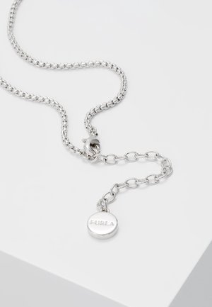 Sølvkæde med justerbare led og en rund vedhæng med indgraveret "FURLA" nær karabinlås, på en hvid overflade.