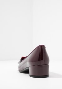 Burgundské lakové boty s nízkým blokovým podpatkem a zaoblenou špičkou. Na přední straně mají ozdobnou mašli a hladký povrch.