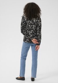 Chemise noire à fleurs à manches longues avec une coupe ample, assortie à un jean droit bleu clair et des ballerines noires, vue de l'arrière.