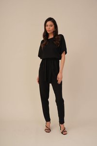 Fekete overál laza szabással, széles ujjakkal és öves derékkal. Fekete magassarkú szandállal viselve, a szövet sima tapintású.