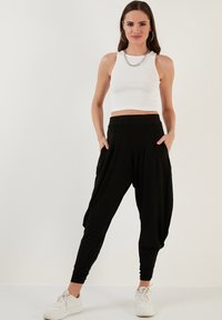 Zwarte harempants met een relaxed fit en taps toelopende manchetten, gecombineerd met een aansluitend wit geribbeld crop top en witte sneakers. Zilveren ketting.