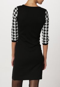 Robe noire avec des manches trois-quarts à motif pied-de-poule. Confectionnée en tissu doux, elle présente un col rond et une silhouette simple.