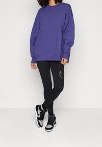 Sudadera morada extragrande, leggings negros con detalle de media luna dorada y zapatillas altas negras con acentos grises.