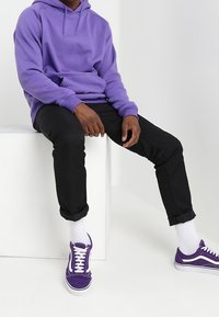 Fialová fleecová mikina s kapucí a přední kapsou, černé slim-fit kalhoty a fialové tenisky s bílými doplňky. Viditelné bílé ponožky.