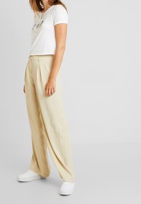 White short-sleeve top with floral embroidery, paired with beige pleated wide-leg trousers and white sneakers. Simple, casual outfit.