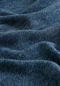 Tela de mezclilla en azul oscuro, que presenta un patrón texturizado y tejido con fibras visibles y ligeras variaciones de color, drapeada y arrugada.