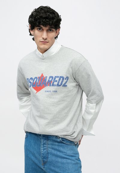 Hall hallipluus sinise ja punase DSQUARED2 logoga, ümara kaelusega. Kanditud valge kraega särgi peal. Sinised teksad taskutega. Ühtlane taust.