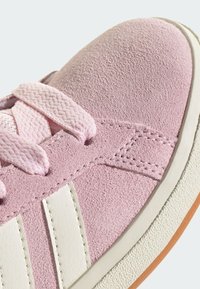 Baskets en daim rose avec des rayures en cuir blanc et une semelle en caoutchouc texturée. Elles disposent de lacets plats et de coutures le long du bord.