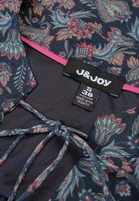 Navy top met bloemenpatroon en een roze accent langs de kraag. Beschikt over een strikdetail en een label met maat S (38) en het merk J&JOY.