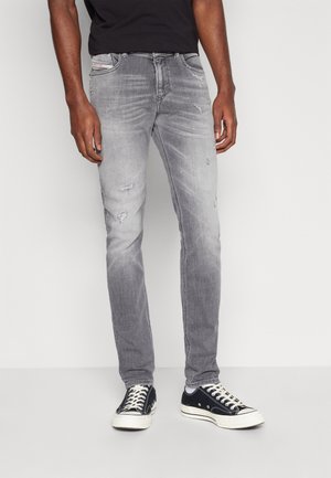 Jeans grises para hombre con un lavado desgastado, que presentan detalles desgastados y un ajuste Slim. Combinados con zapatillas de lona en blanco y negro.