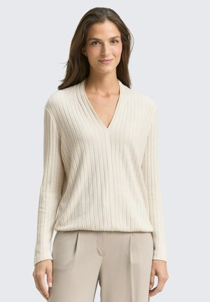 Pull en V à manches longues beige texturé à côtes, présentant une coupe décontractée et une texture douce, associé à un pantalon beige clair.