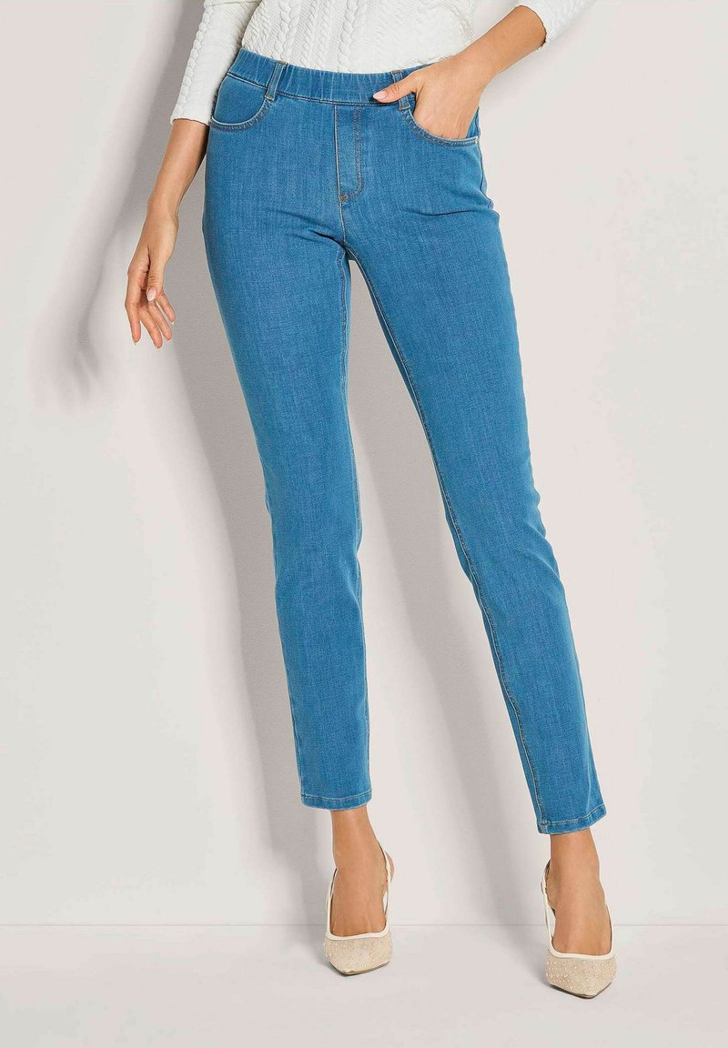 Lichtblauwe denim broek met een elastische tailleband, twee vo Taschen en een slim-fit ontwerp, gecombineerd met neutraal gekleurde hoge hakken.