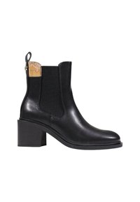 Botín de cuero negro hasta el tobillo con un panel elástico texturizado y acento de corcho en la parte posterior. Tacón cuadrado con un acabado suave.