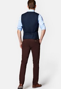 Granatowa kamizelka, jasnoniebieska koszula, brązowe spodnie. Kamizelka ma detal do regulacji z tyłu. Brązowe buty dopełniają outfit.