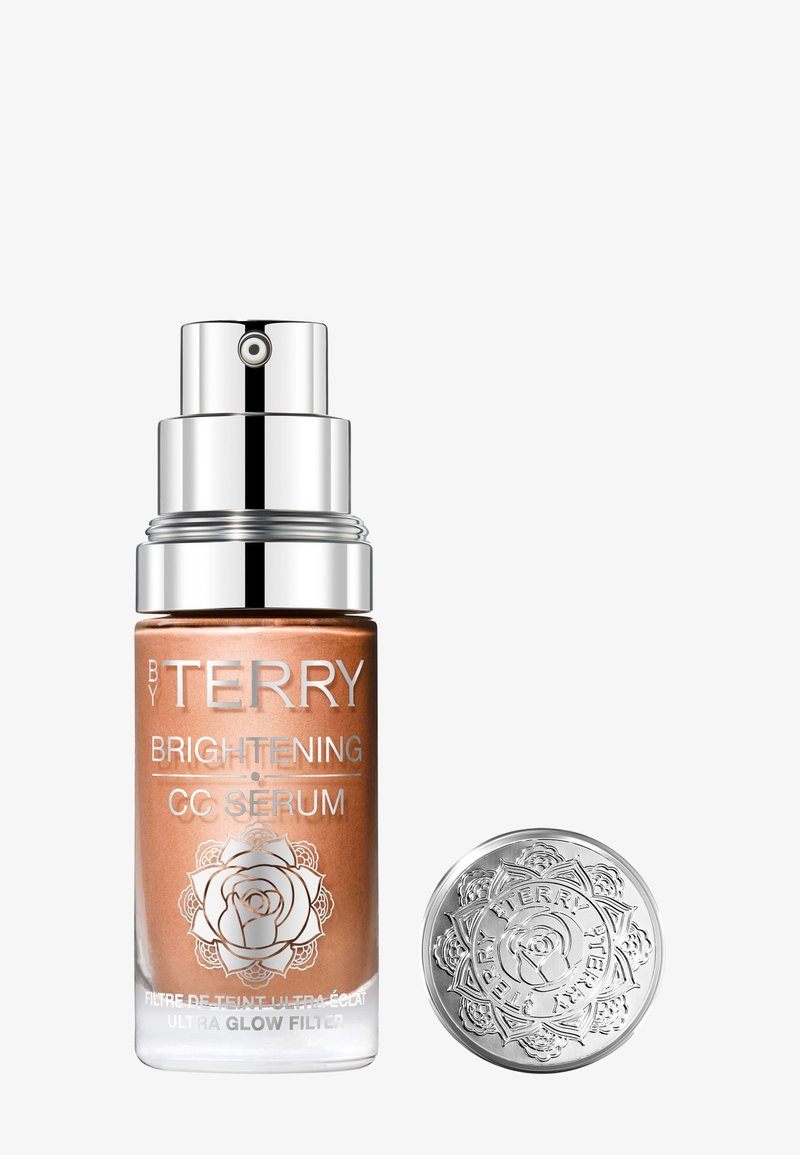 Flacon de sérum éclaircissant By Terry avec pompe argentée et capuchon décoratif argenté à côté, sur fond blanc.
