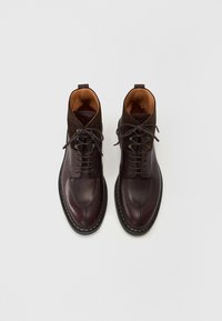 Bottines en cuir et suède marron avec un bout rond, fermeture à lacets, intérieur contrasté beige, et coutures le long de la semelle.