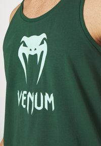 Canotta verde in cotone con una grande grafica bianca di una testa di serpente e la parola "VENUM" in un carattere stilizzato sottostante.